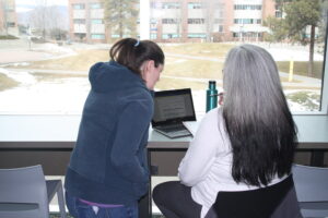 Two indigenous students from the Metis and Fort McKay First Nations in front of a laptop studying at a common space on campus.