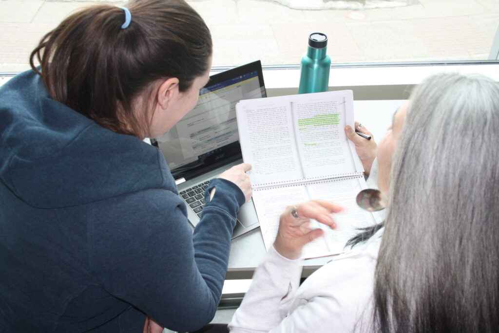 Two indigenous students from the Metis and Fort McKay First Nations studying at a campus common space. The student that is on the left is pointing to the other student notes.