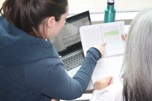 Two Indigenous students from the Metis and Fort McKay First Nations studying in a campus common space. The student that is on the left is pointing to a highlighted section in the other student's notes.