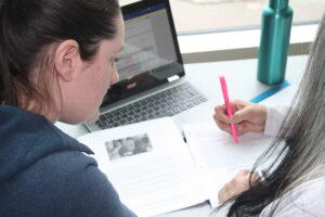 Two Indigenous students from the Metis and Fort McKay First Nations studying in a common space on campus. One of the students is highlighting their notes while the other one watches.