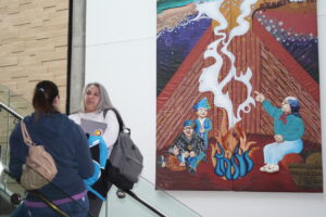 Two Indigenous students from the Metis and Fort McKay First Nations talking on the stairs of a common space on campus. An art piece is on the wall in the background.