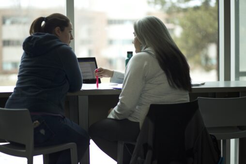 Two Indigenous students from the Metis and Fort McKay First Nations talking and studying in front of a laptop in a common space on campus.