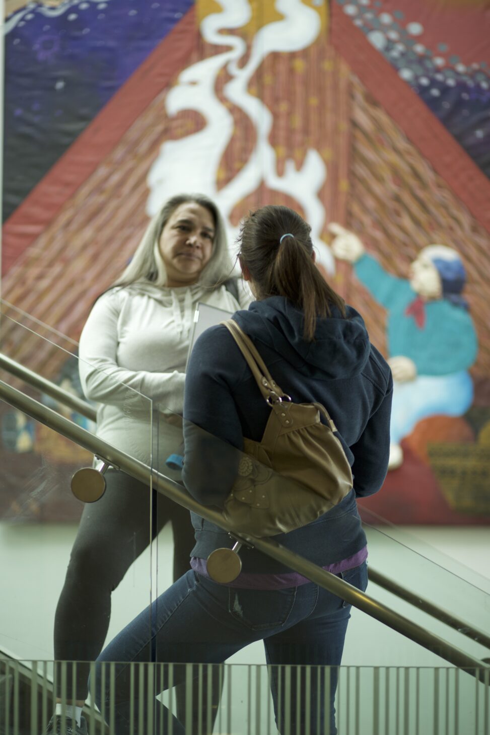 Two Indigenous students from the Metis and Fort McKay First Nations talking while standing on stairs in a common space on campus.