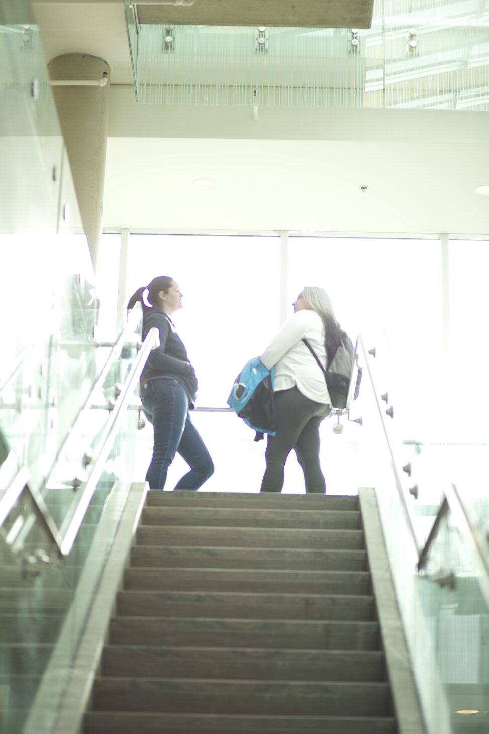 Two Indigenous students from the Metis and Fort McKay First Nations talking at the top of a staircase in a campus common space.