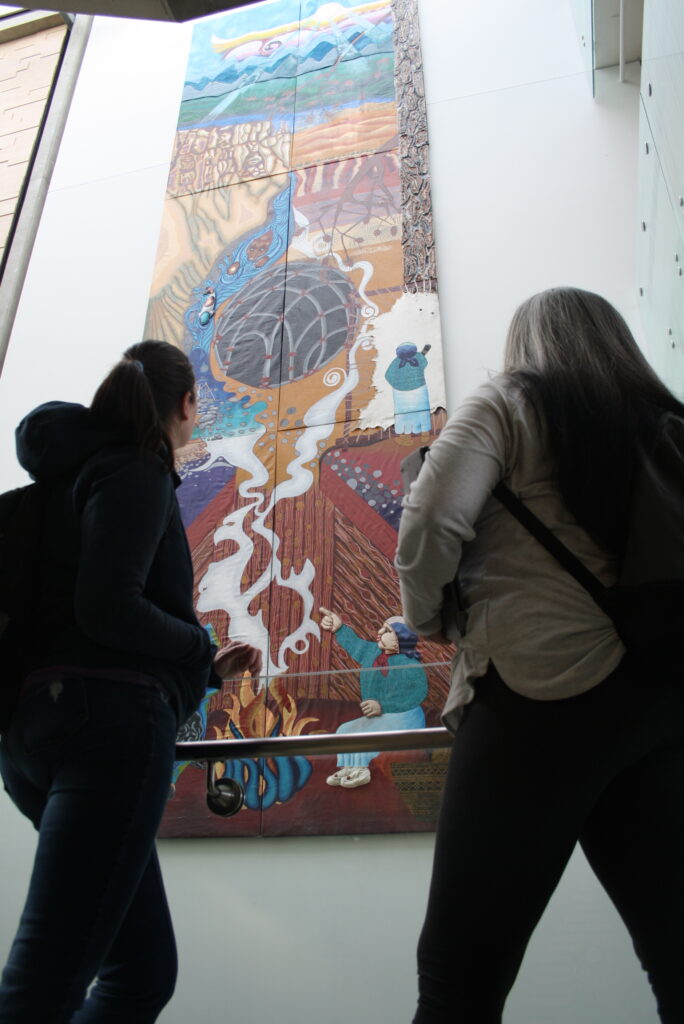 Two indigenous students talking about the piece of art that is in front of them. Students from the Metis and Fort McKay First Nations.