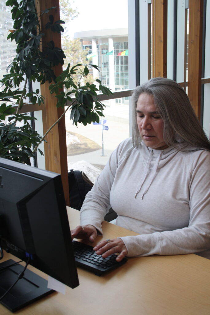 Indigenous student studying using a computer in a common space on campus.