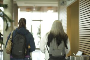 Two Indigenous students from the Metis and Fort McKay First Nations walking down a hallway in a campus building.