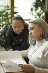 Two Indigenous students from the Stat'imc/Nlaka'pamux and Fort McKay First Nations studying by reading a notebook in a campus library.