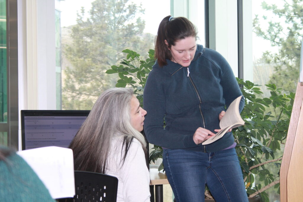 Two Indigenous students studying at a library on campus. One student is showing an open book to the other student.