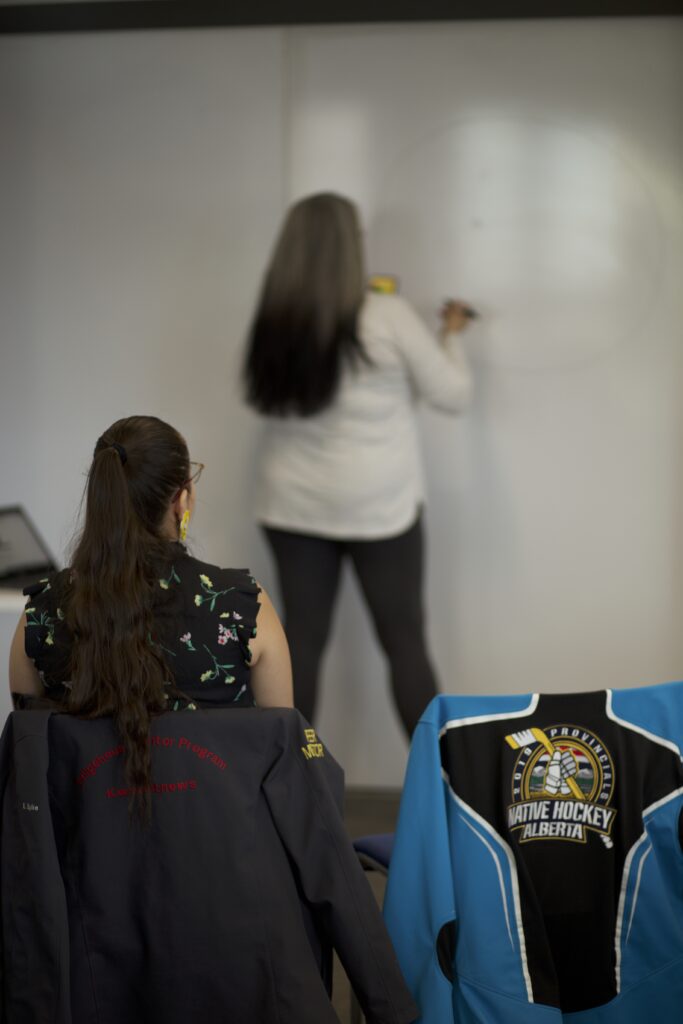 Indigenous student from the Fort McKay First Nation tutoring students from the St'at'imc/Nlaka'pamux Nation in front of a whiteboard.