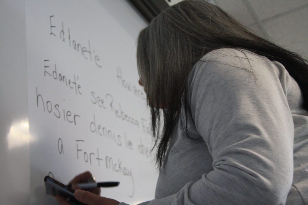 Indigenous teacher from the Fort McKay First Nation teaching an Indigenous language by writing on a whiteboard.