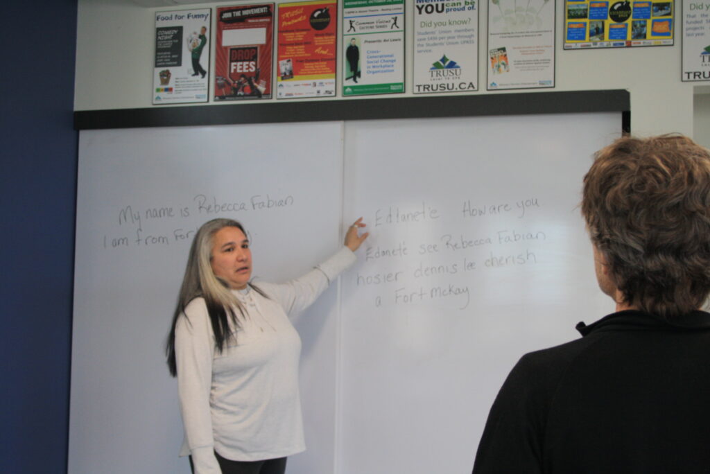 Indigenous teacher from the Fort McKay First Nation teaching an Indigenous language. The teacher is explaining something on a whiteboard to a student.