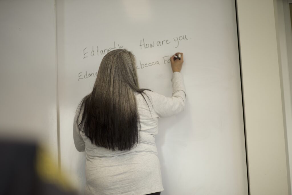 Indigenous teacher from the Fort McKay First Nation teaching an Indigenous language class by writing on a whiteboard.