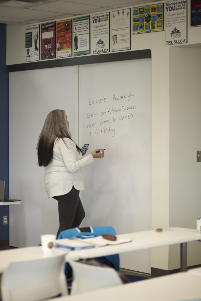 Indigenous teacher from the Fort McKay First Nation teaching an Indigenous language by copying something from their phone onto a whiteboard.