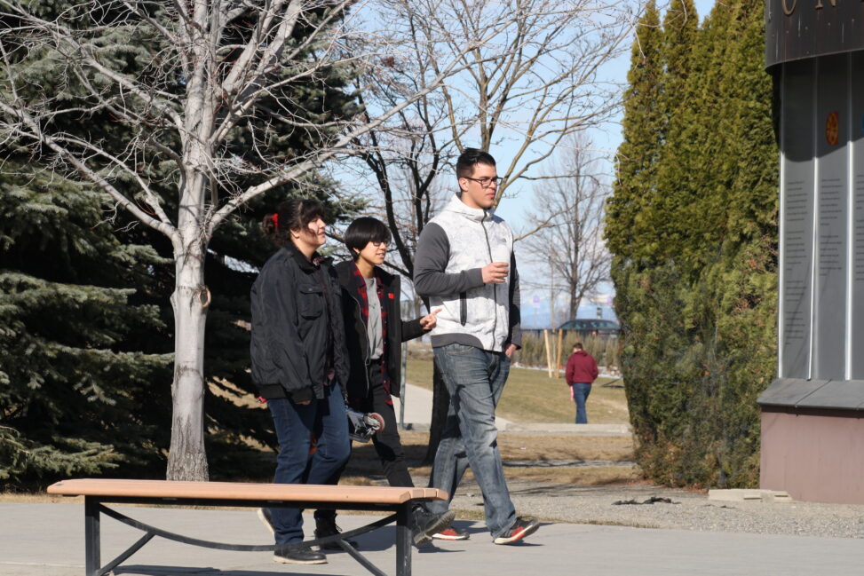 Three Indigenous students from the Haida and Ntekepmx Nations walking outside on campus.