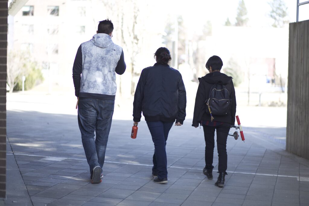 Three Indigenous students from the Haida and Ntekepmx Nations walking away from the camera outdoors on a campus.