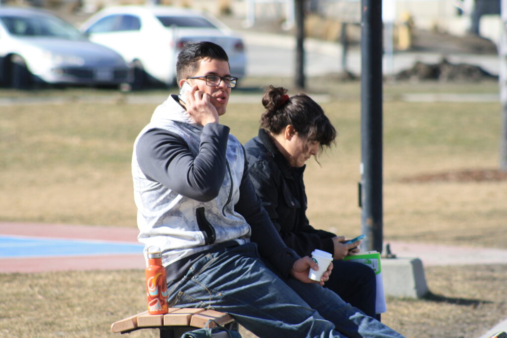 Two Indigenous students from the Ntekepmx and Haida Nations sitting on an outdoor campus bench.