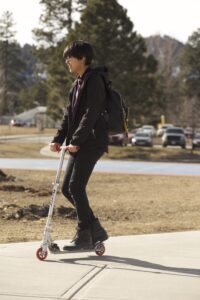 Indigenous student from the Ntekepmx Nation riding a scooter outside on campus.