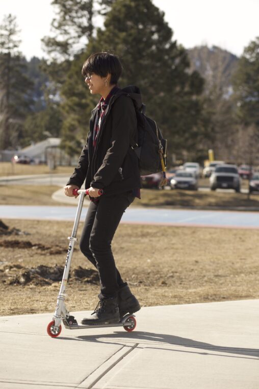 Indigenous student from the Ntekepmx Nation riding a scooter outside on campus.