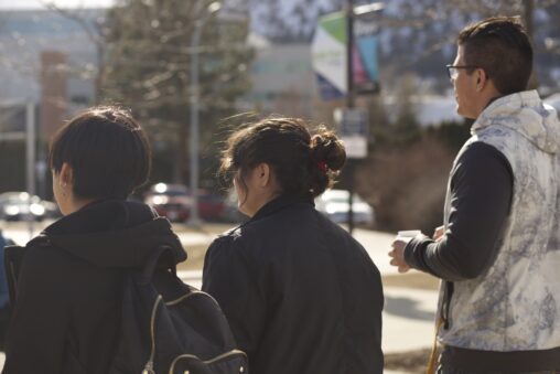 Three indigenous students from the Haida and Ntekepmx Nations walking on campus outdoors.