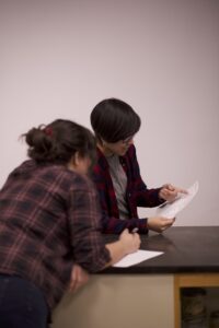 Two Indigenous students talking and taking notes in a campus common space.