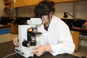 Indigenous student from the Ntekepmx Nation looking through a microscope while adjusting its lens in a science laboratory.