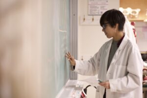 Indigenous student with glasses from the Ntekepmx Nation writing on a chalkboard in a biology laboratory.