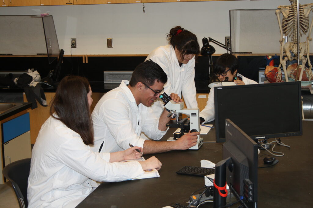 Four Indigenous students from the Metis, Haida, and Ntekepmx Nations using two microscopes in a biology laboratory.