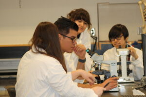 Four Indigenous students from the Metis, Haida, and Ntekepmx Nations using two microscopes in a biology laboratory.