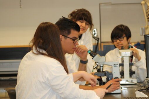 Four Indigenous students from the Metis, Haida, and Ntekepmx Nations using two microscopes in a biology laboratory.