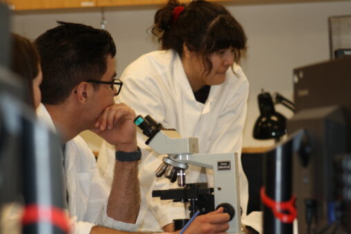 Three Indigenous students from the Haida, Ntekepmx, and Metis Nations with a microscope in a science laboratory.