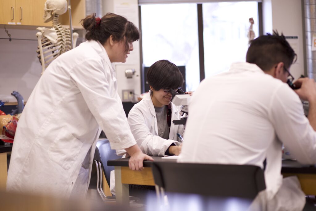 Three Indigenous students from the Haida and Ntekepmx Nations using two microscopes in a biology laboratory.