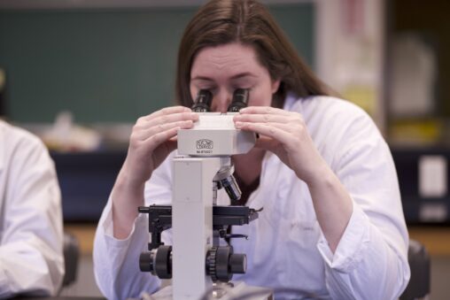 Indigenous student holding microscope with both hands while using it in a science/biology laboratory.