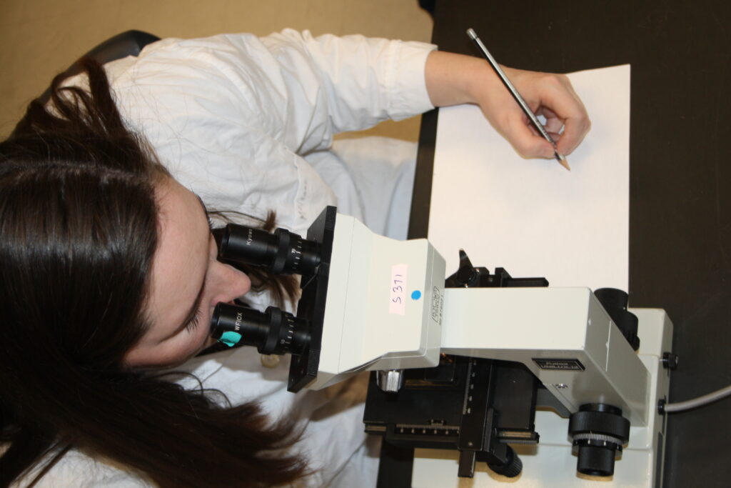 Indigenous student from the Metis Nation looking through a microscope and taking notes in a biology laboratory.