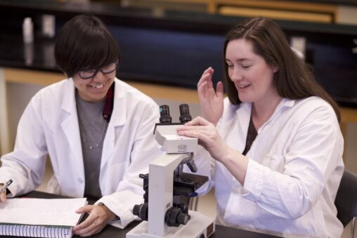 Two Indigenous students from the Metis and Ntekepmx Nations sitting in front of a microscope in a biology laboratory.