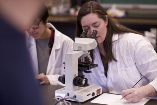 Two Indigenous students from the Metis and Ntekepmx Nations using a microscope in a biology laboratory.