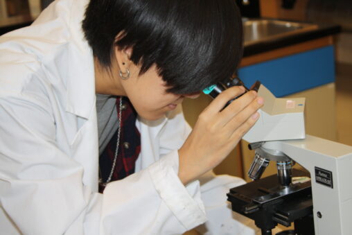 Indigenous student from the Ntekepmx Nation holding a microscope eyepiece while looking through it in a biology laboratory.