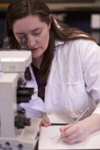 Indigenous student from the Metis Nation using a microscope while taking notes in a biology laboratory.