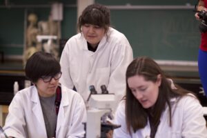 Three Indigenous students from the Metis and Ntekepmx Nations gathered around microscope in a biology laboratory.