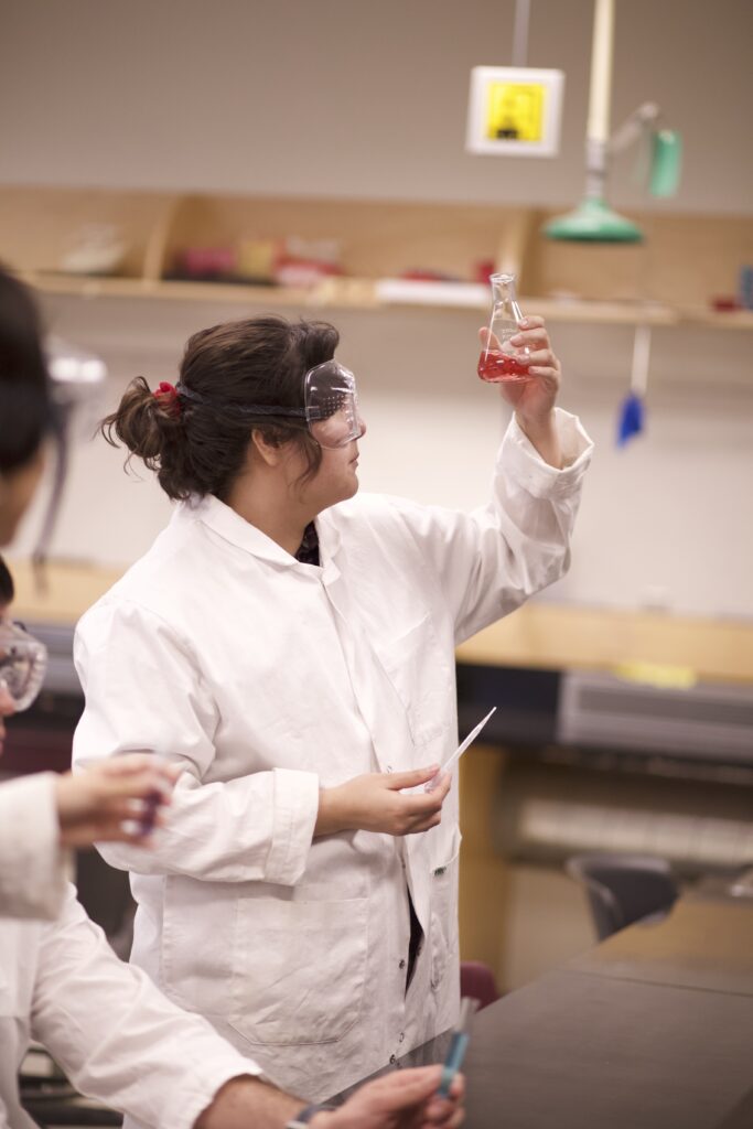 Indigenous student holding an Erlenmeyer flask to examine the liquid inside in a chemistry laboratory.