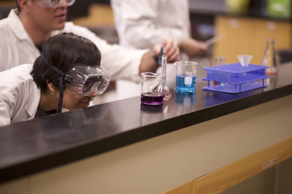 Indigenous students from the Ntekepmx and Haida Nations measuring liquids in Erlenmeyer flasks in a chemistry laboratory.