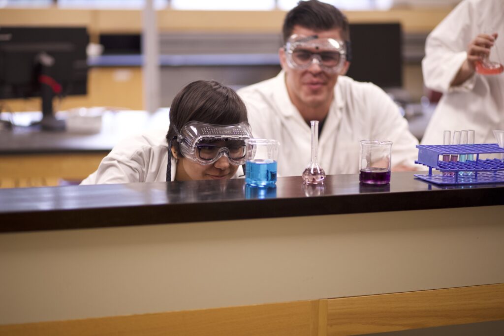 Indigenous students from the Haida and Ntekepmx Nations examining liquid inside two beakers and one flask in a chemistry laboratory.