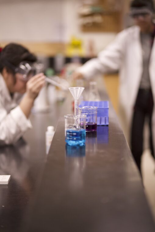 Chemistry glassware with two Indigenous students out of focus in the background in a chemistry laboratory.