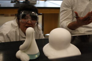 Indigenous student from the Ntekepmx Nation observing a chemical reaction that is producing foam in a chemistry laboratory. Another Indigenous student sits beside the other student slightly off camera.