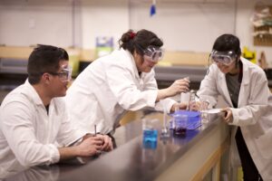 Three Indigenous students from the Haida and Ntekepmx Nations conducting an experiment using chemistry glassware in a chemistry laboratory.