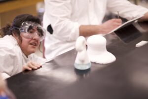 Indigenous student from the Ntekepmx Nation observing a chemical reaction while another student takes notes in a chemistry laboratory