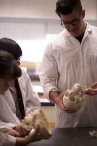 Three Indigenous students from the Haida and Ntekepmx Nations in an anatomy lab. Two students are holding skull props while the third one is observing.