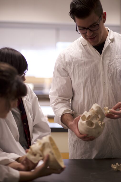 Three Indigenous students from the Haida and Ntekepmx Nations in an anatomy lab. Two students are holding skull props while the third one is observing.