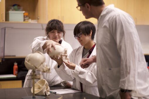 Three indigenous students from the Haida and Ntekepmx Nations in an anatomy lab. Two students are holding a skull while the third student is observing.