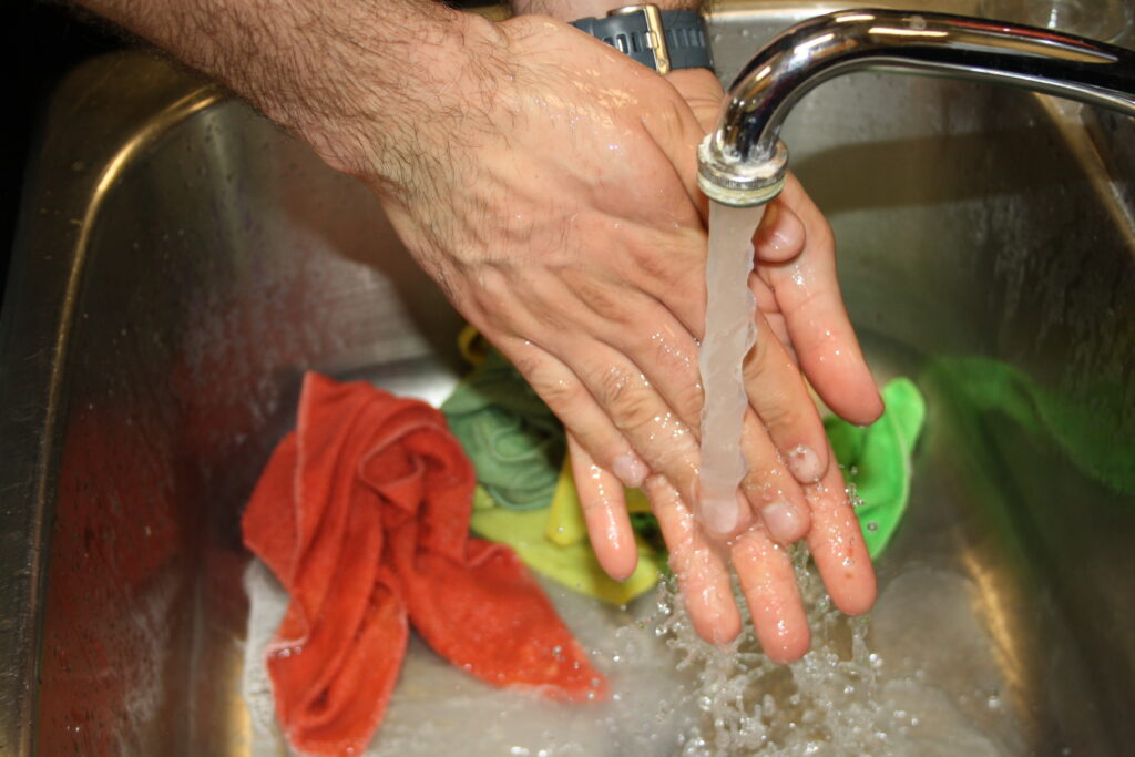 Washing hands on sink. The water is running over some colorful towels that are on the sink.